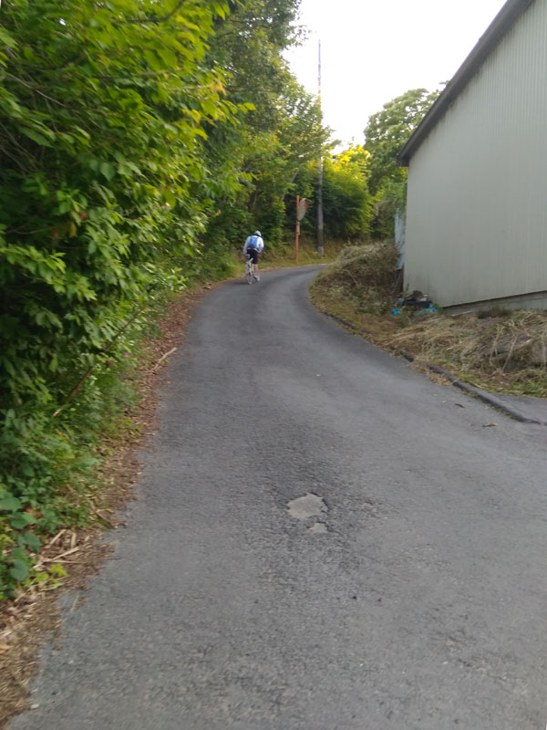 A road cyclist pushing his bike up a hill in the distance