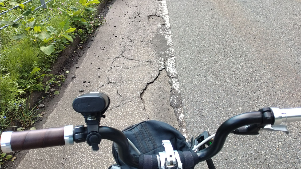 Cracked asphalt shoulder with potholes - typical Hokkaido road condition after winter snow removal