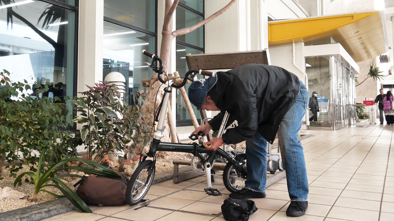 Bicycle assembly area at Naha Airport - open space near bus stops with tropical vegetation