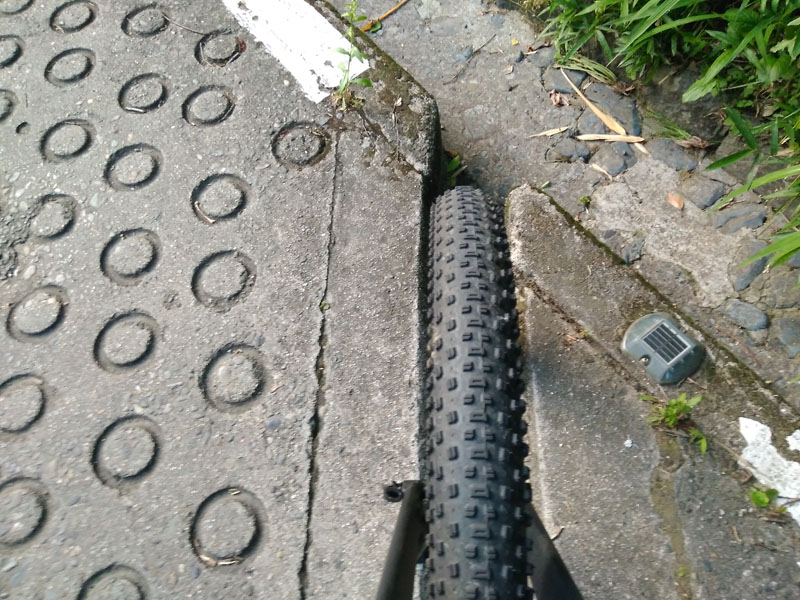 A wide drainage trench running across the steep road, perfectly swallowing a large MTB tire